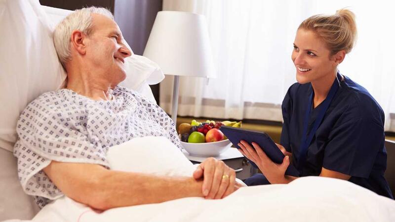 One caregiver and a care taker smiling and talking by the bed