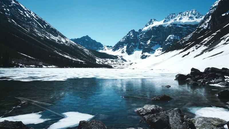 An image showing beautiful snowy mountain tops and a semi frozen lake