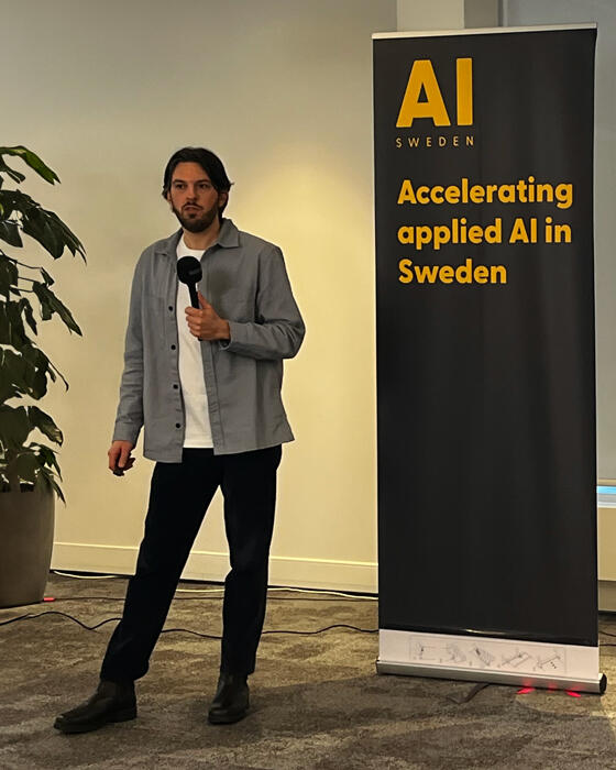 a picture of Jonathan Permert with a microphone in front of an AI Sweden banner